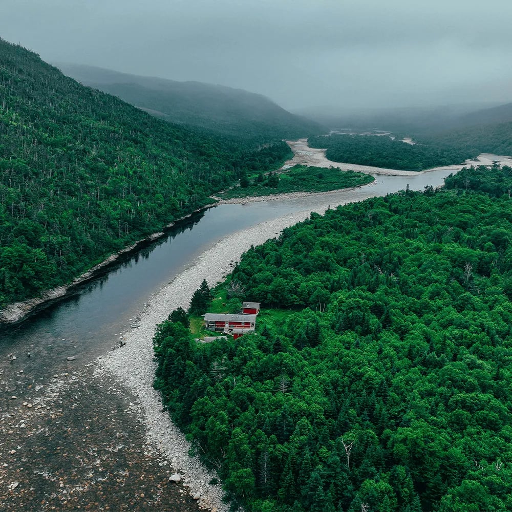 Aerial view of Salmon Hole Lodge buildings nestled by a winding river in a green valley