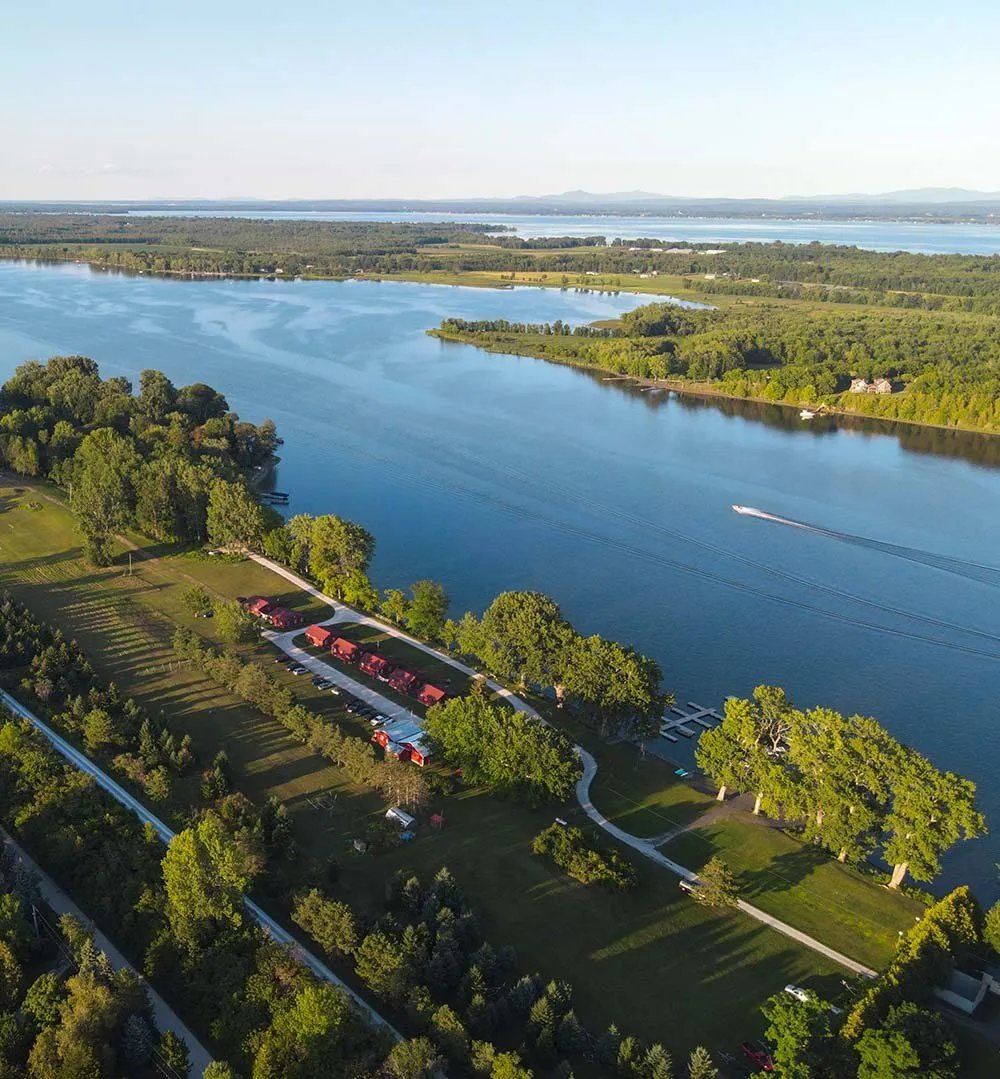 Aerial view of red-roofed cottages along a riverbank with a boat wake on the water