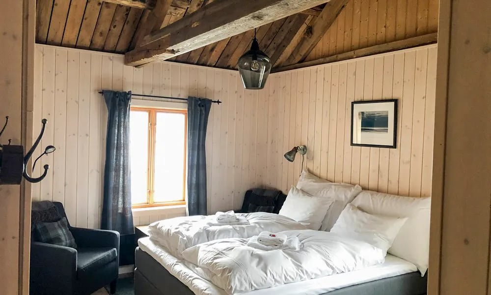 Cozy bedroom with light wood paneling, exposed wooden beams, and a double bed with white linens
