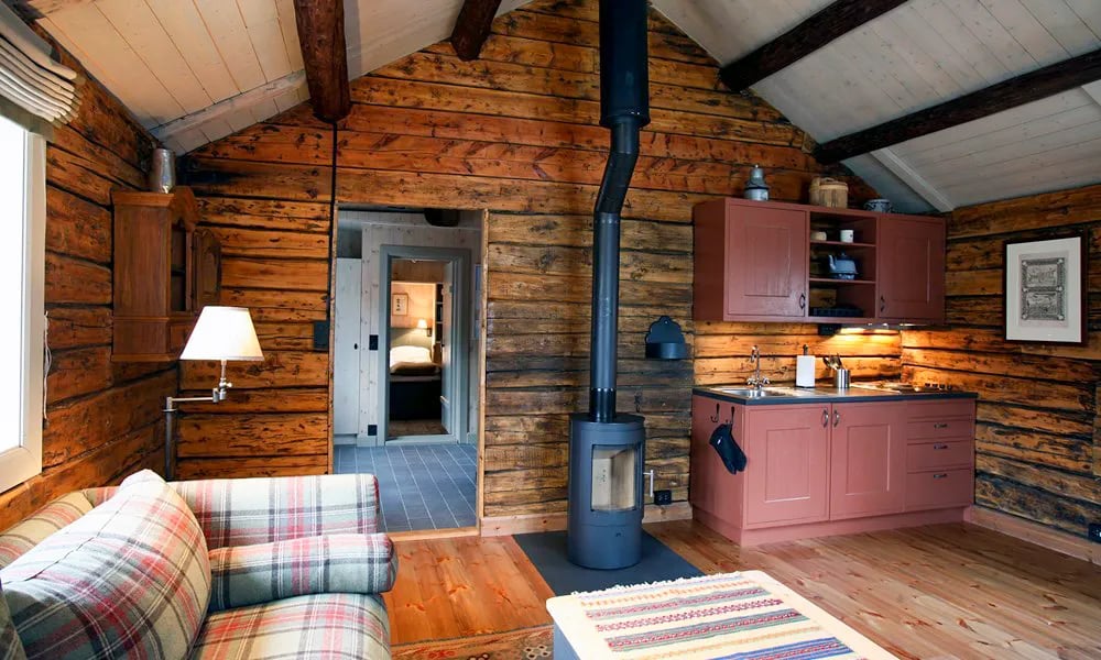 Living area with a plaid sofa, a wood-burning stove, and a small kitchenette in a rustic cabin