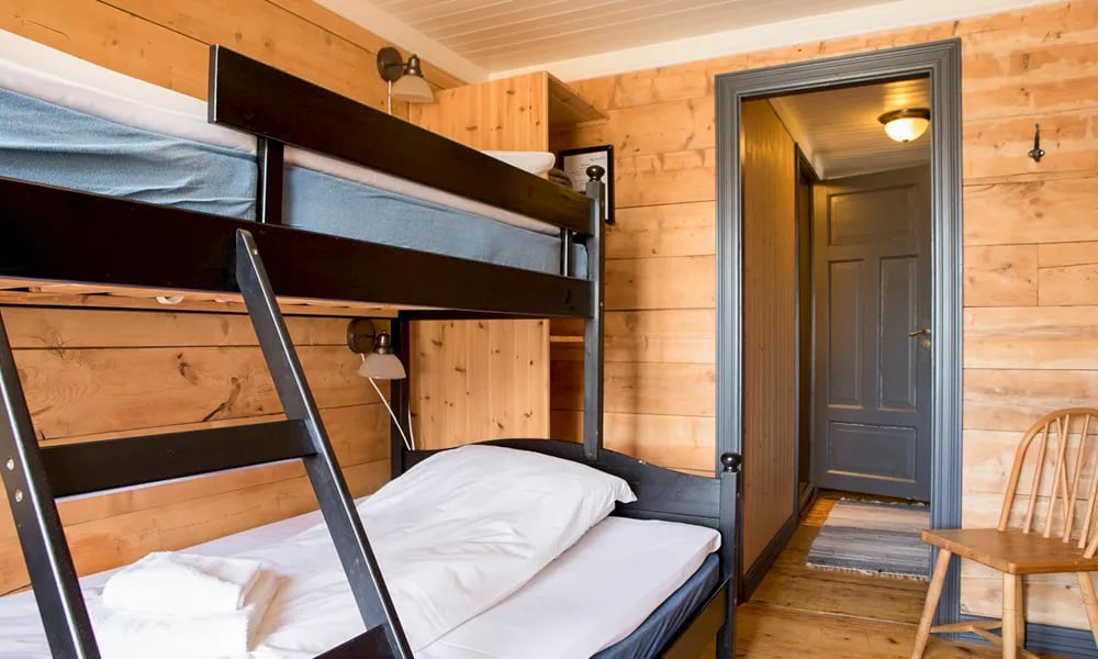 Bedroom with a black bunk bed, wooden walls, and an open doorway leading to another room