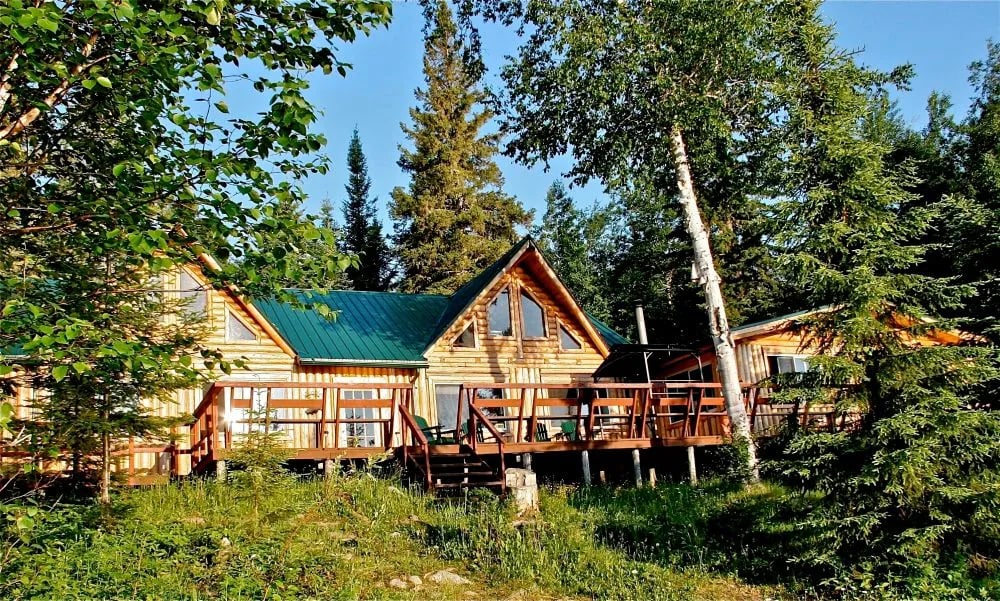 Main lodge building with green roof and large deck surrounded by summer trees