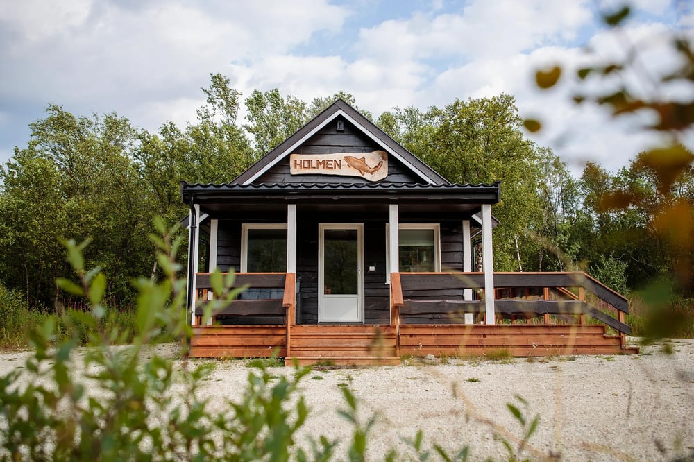 Small dark wood cabin with a covered porch and two white Adirondack chairs.
