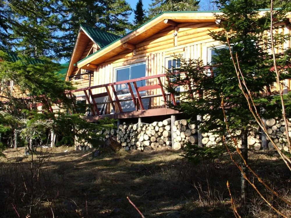 Rustic log cabin exterior with a deck and stacked firewood underneath