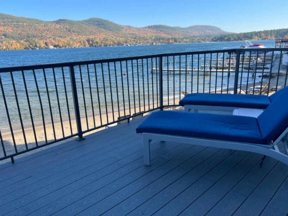 Outdoor lounge area with dark sofas and tables, overlooking the lake and forested mountains