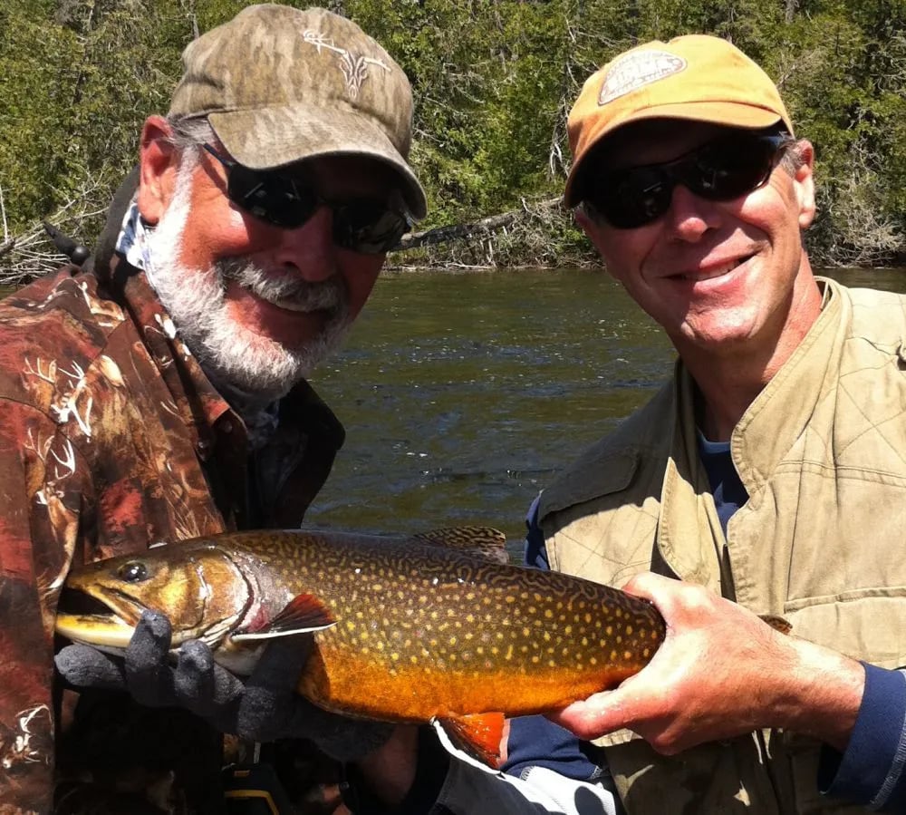 Two smiling anglers holding a large, colorful brook trout together