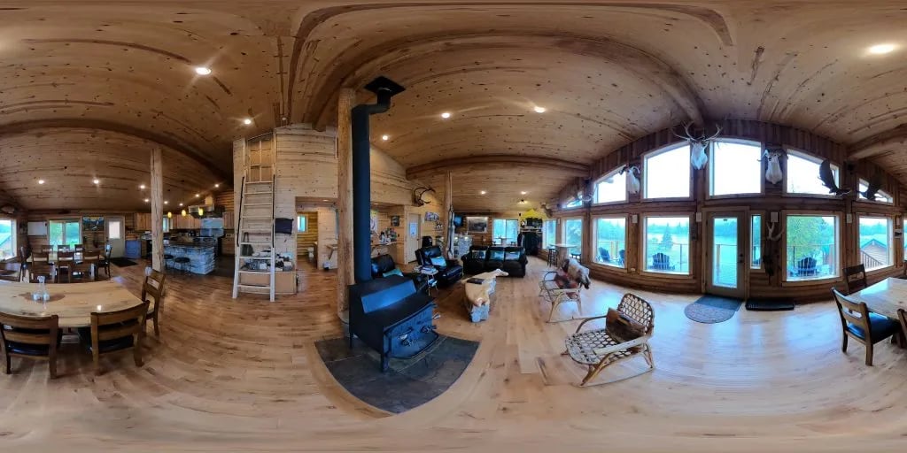 Panoramic view of the main lodge common area with dining tables and a wood-burning stove