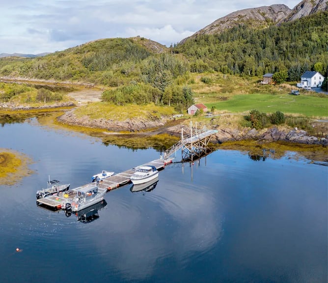 Aerial view of Tjongsfjord Lodge buildings and dock nestled by the fjord, with a large mountain backdrop.