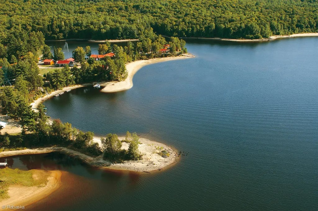 Aerial view of Rabaska Lodge nestled on a forested peninsula by a large lake.