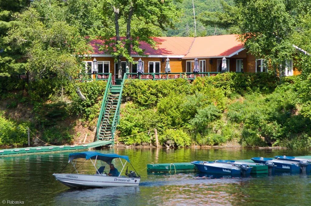 Rabaska Lodge building with a red roof and green stairs, seen from the water with boats docked.