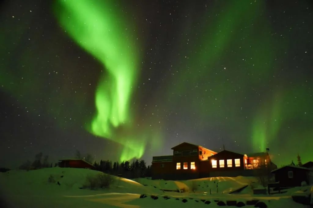 Trout Rock Lodge buildings illuminated under a vibrant green aurora borealis.