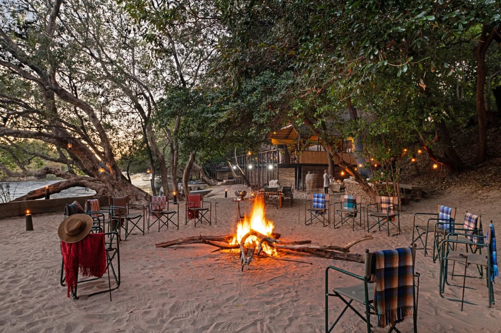 Lodge buildings with thatched roofs nestled among trees along a riverbank.