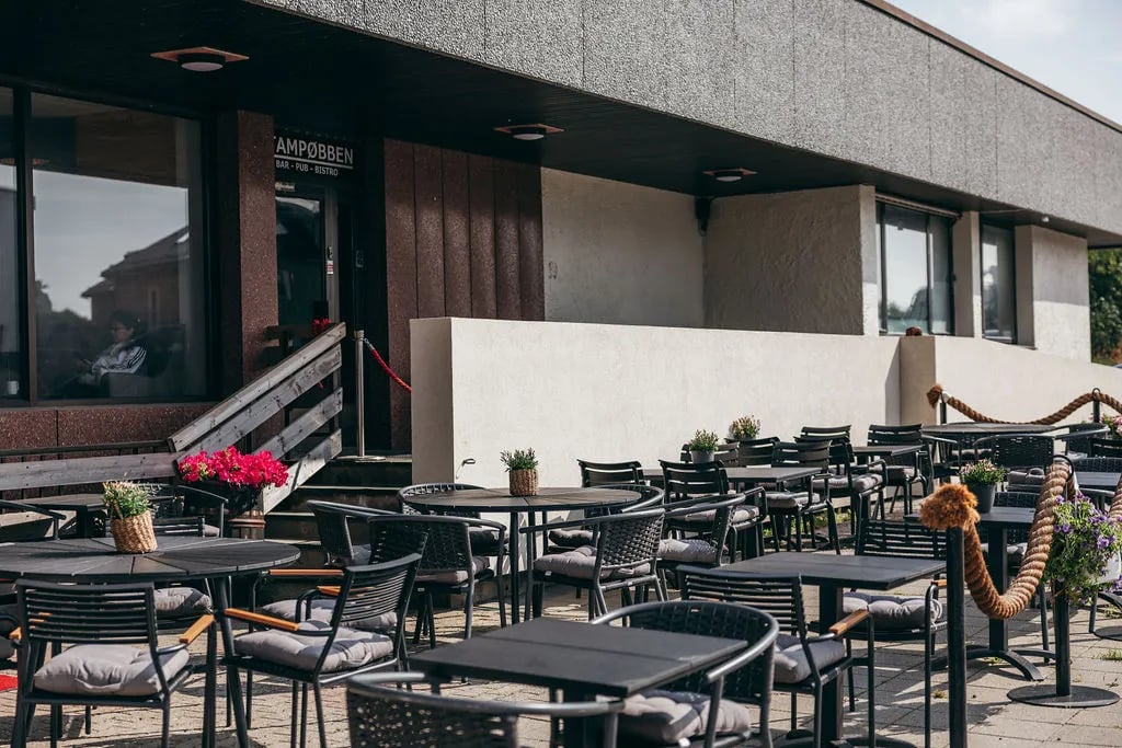 Outdoor patio dining area with black tables and chairs in front of a modern building