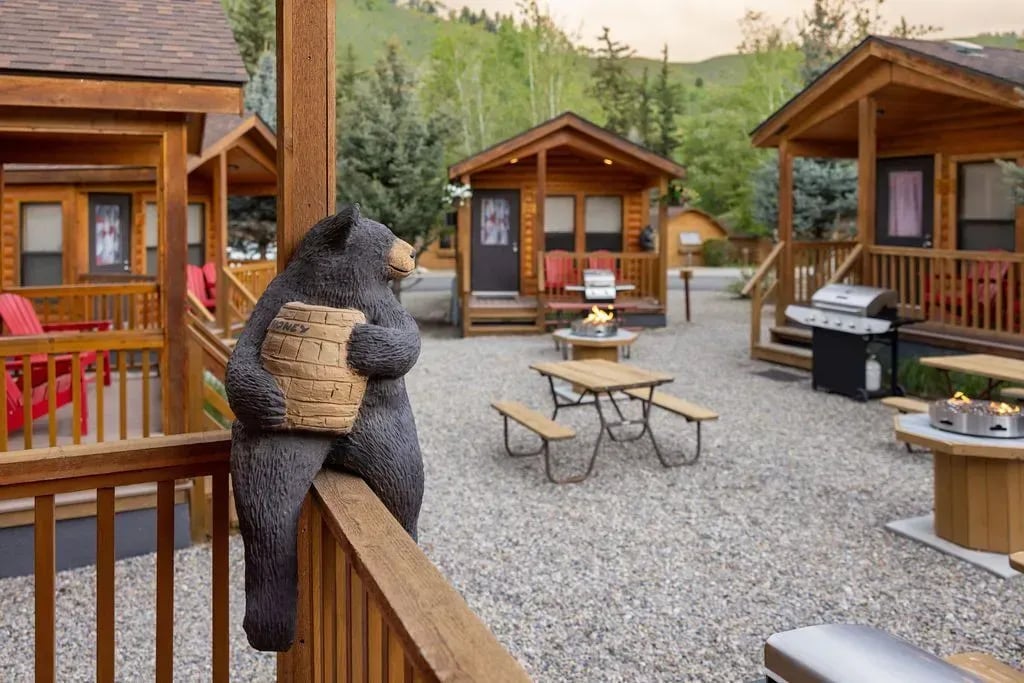 Cluster of rustic log cabins with picnic tables and a bear statue.