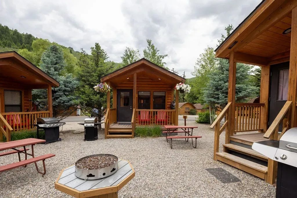 Log cabins surrounding a gravel courtyard with picnic tables and a fire pit.