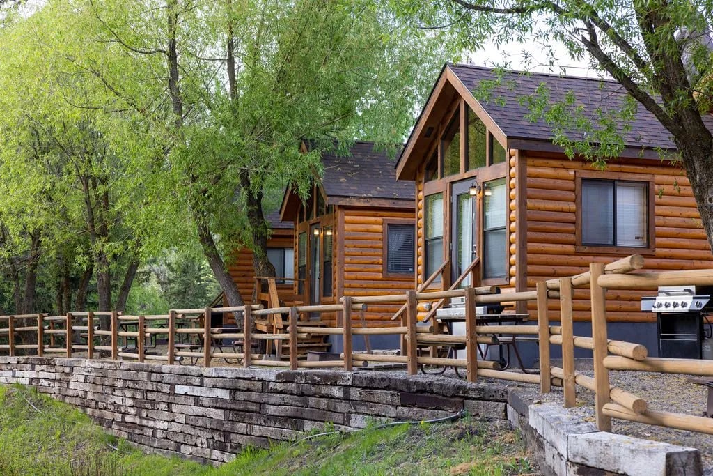 Log cabins situated along a stone wall and wooden fence by the river.