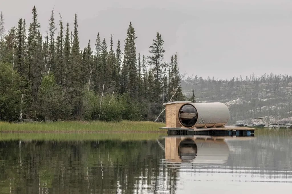 Unique floating barrel cabin with a large round window, surrounded by a calm lake and forest