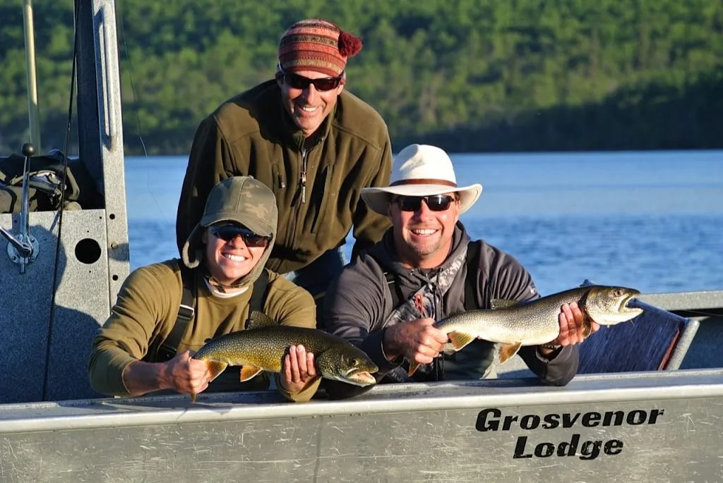 Three happy anglers in a "Grosvenor Lodge" boat holding two lake trout.