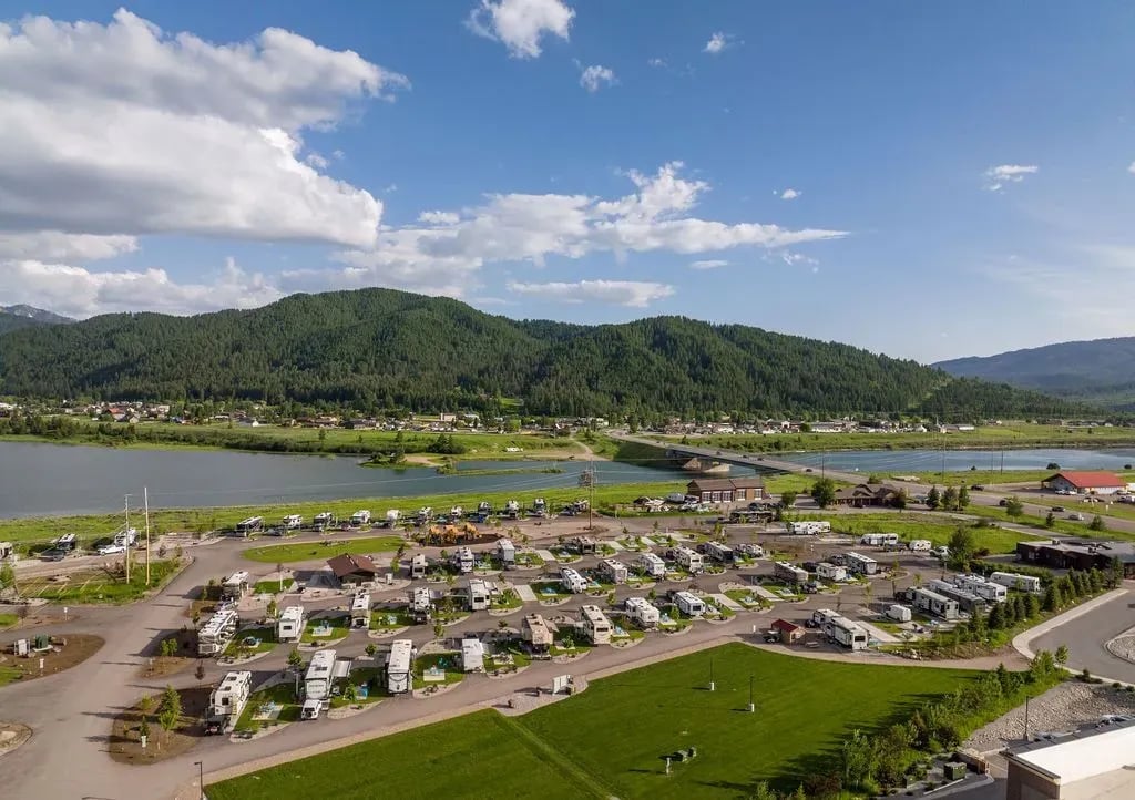 Aerial view of Alpine Valley RV Resort with RVs, green fields, a river, and mountains