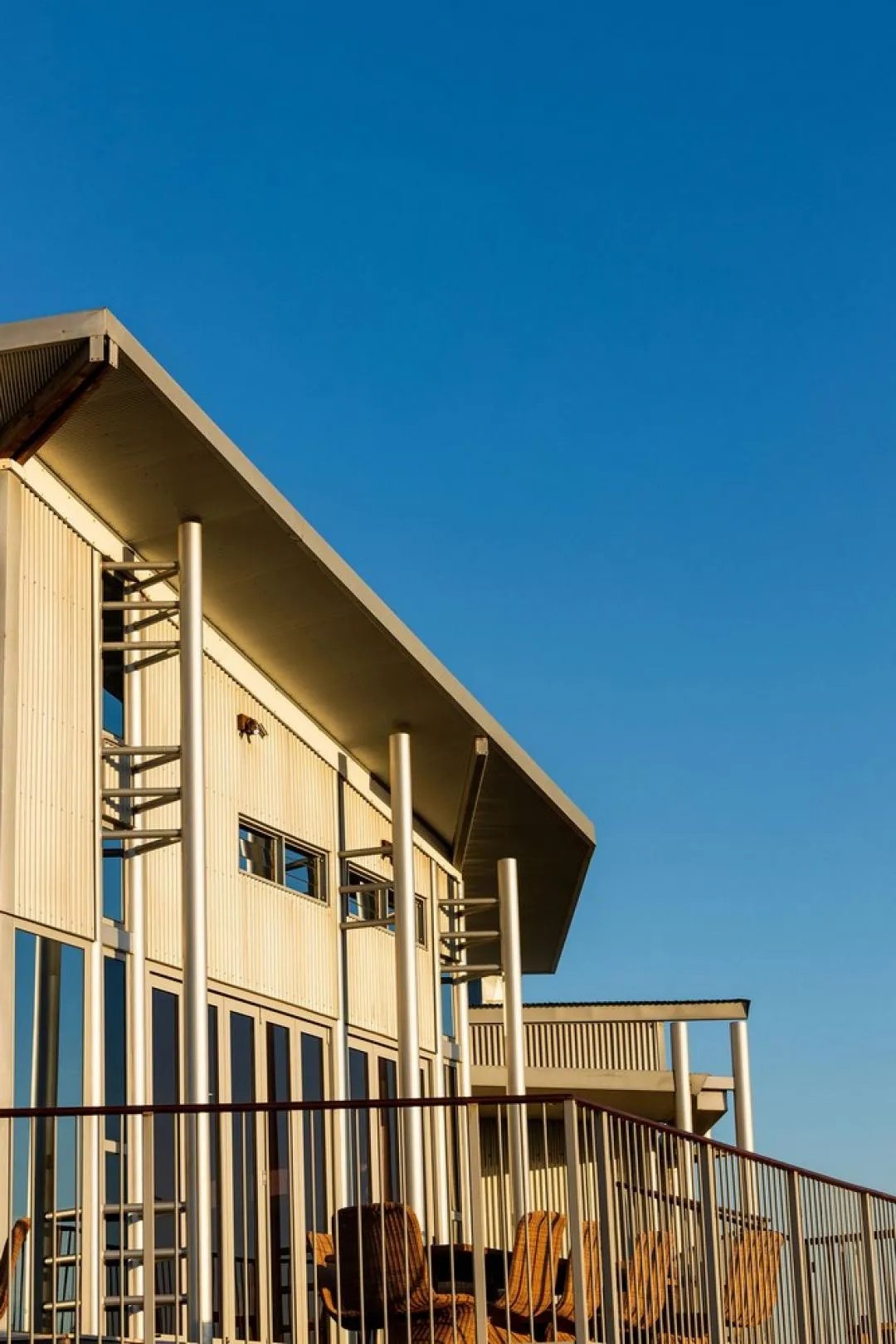 Modern lodge exterior with large windows and a balcony under a clear blue sky