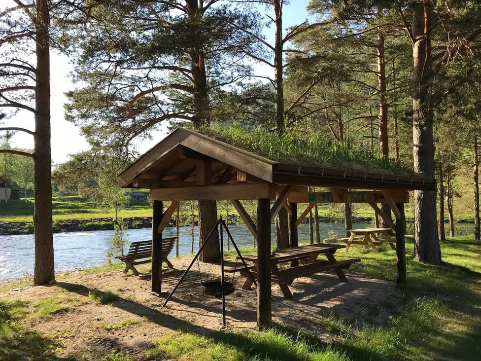 Long wooden bathhouse with a grass roof and a covered porch, surrounded by green trees.
