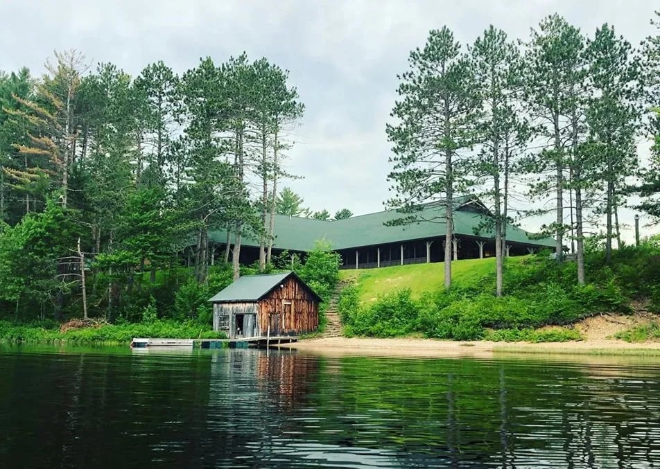 Aerial view of the main lodge building with a green roof next to a blue lake and dense forest