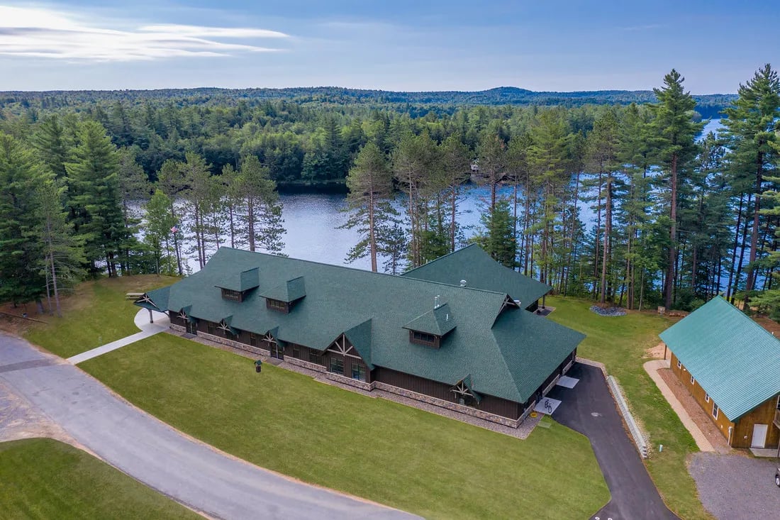 Aerial view of Sentinel Hall lodge with a green roof, surrounded by pine trees and overlooking a lake