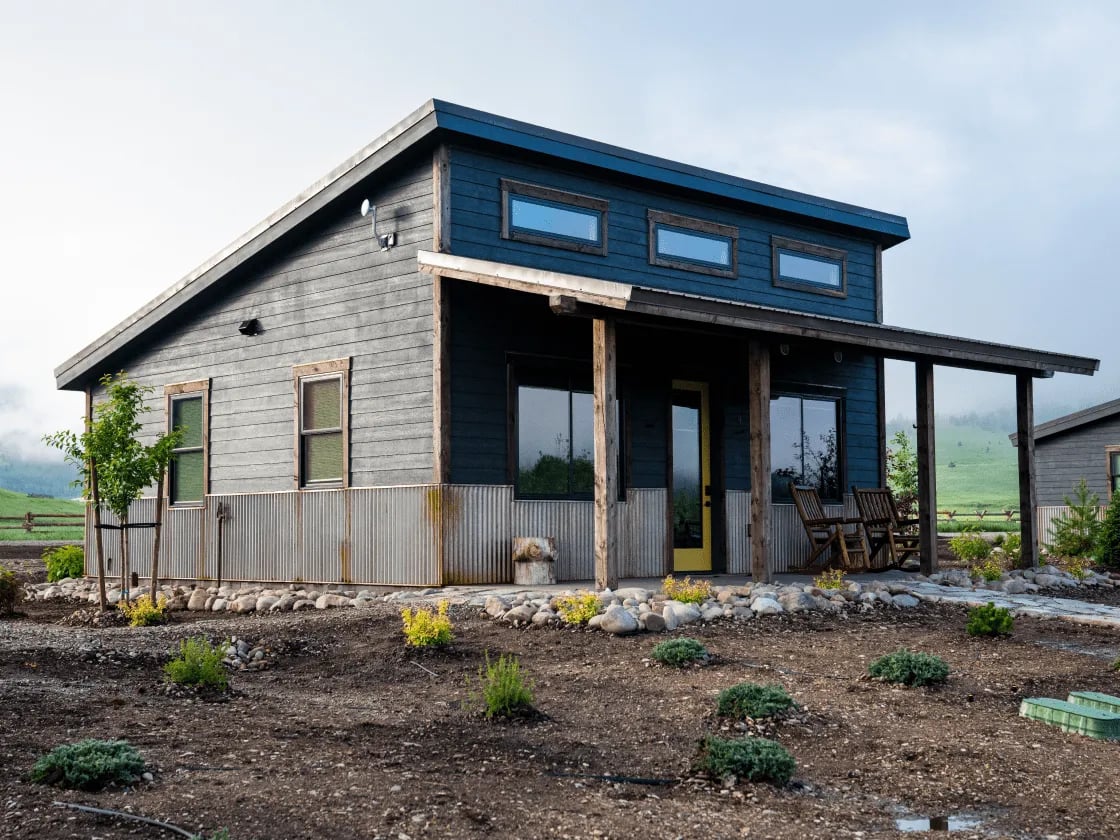 the outside view of a cabin at The Meadows on Rock Creek. The background is foggy with green hills and the front has small bushes growing.