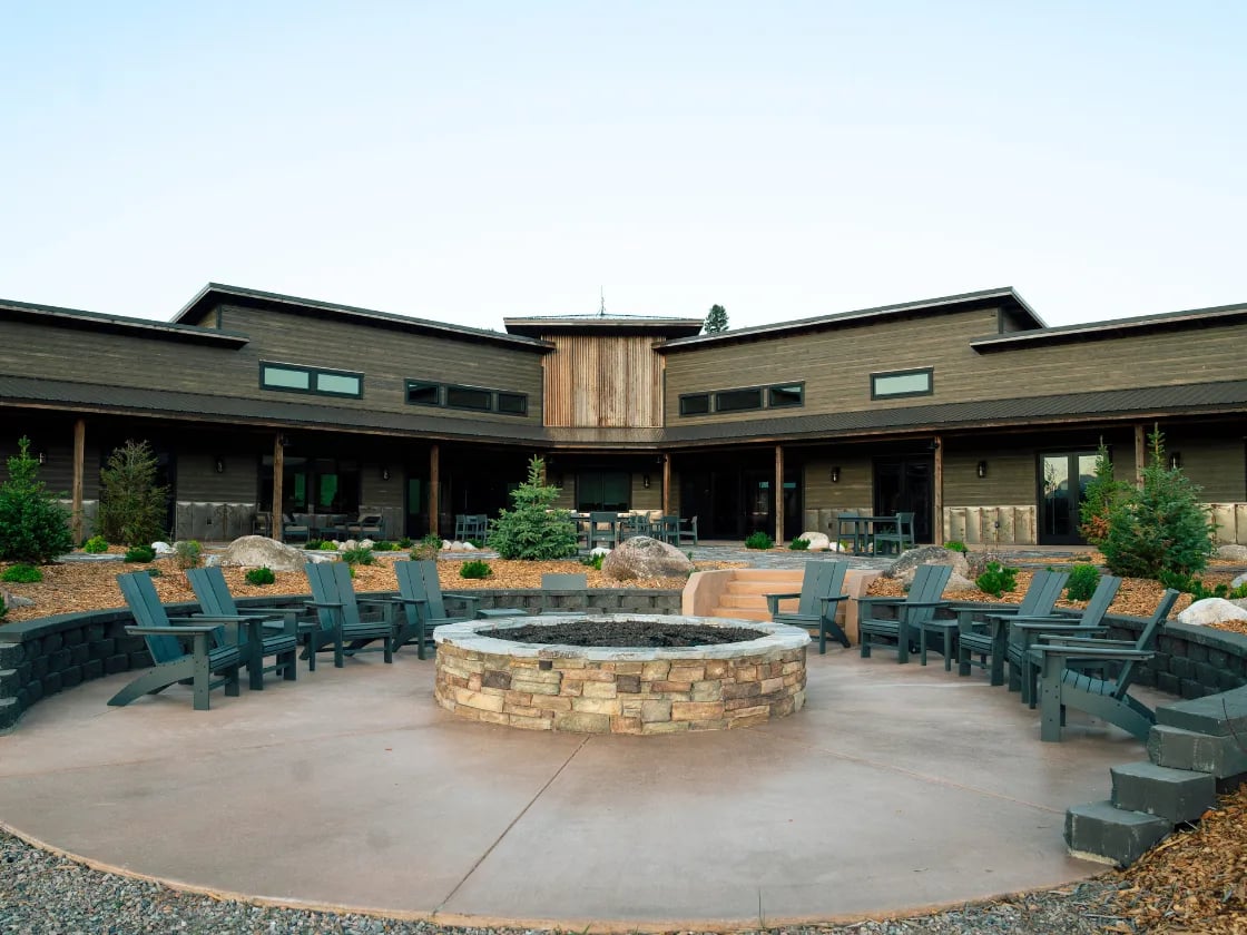 a large brown building with a fire pit and chairs in the courtyard