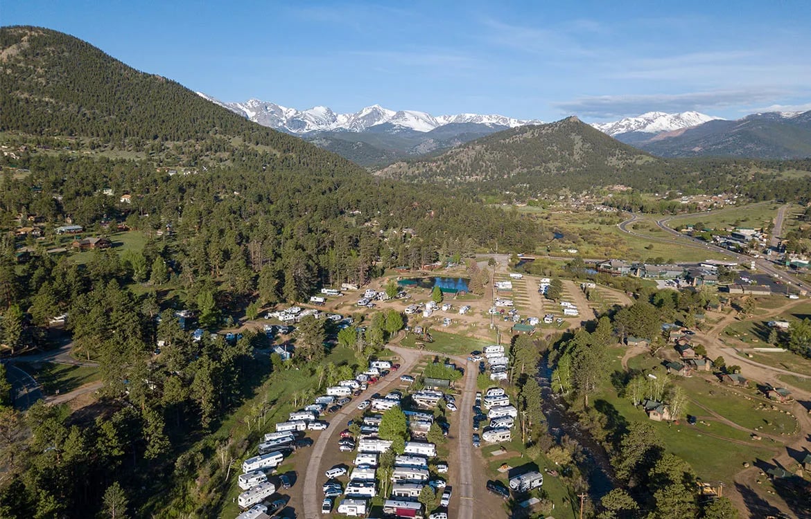 Aerial view of an RV park nestled in a valley surrounded by forested mountains.