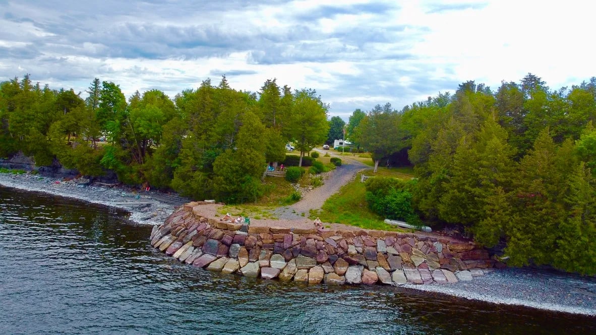 Aerial view of a rocky breakwater and treed shoreline at Champlain Resort Campground.