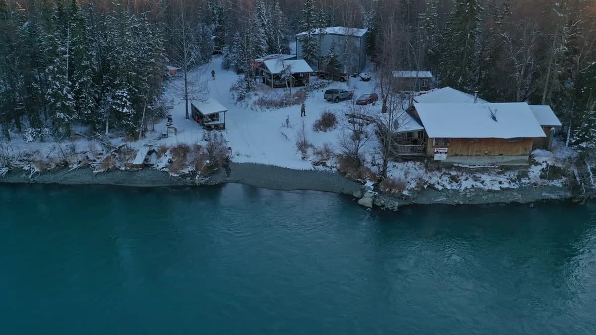 Aerial view of snow-dusted lodge buildings along a riverbank at dusk