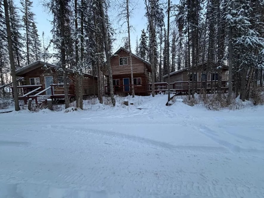 Aerial view of the snow-covered lodge property and cabins along the turquoise river