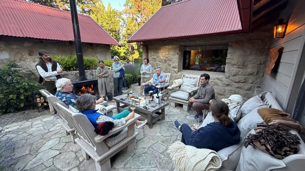 Group of guests gathered around an outdoor fireplace on a stone patio at dusk