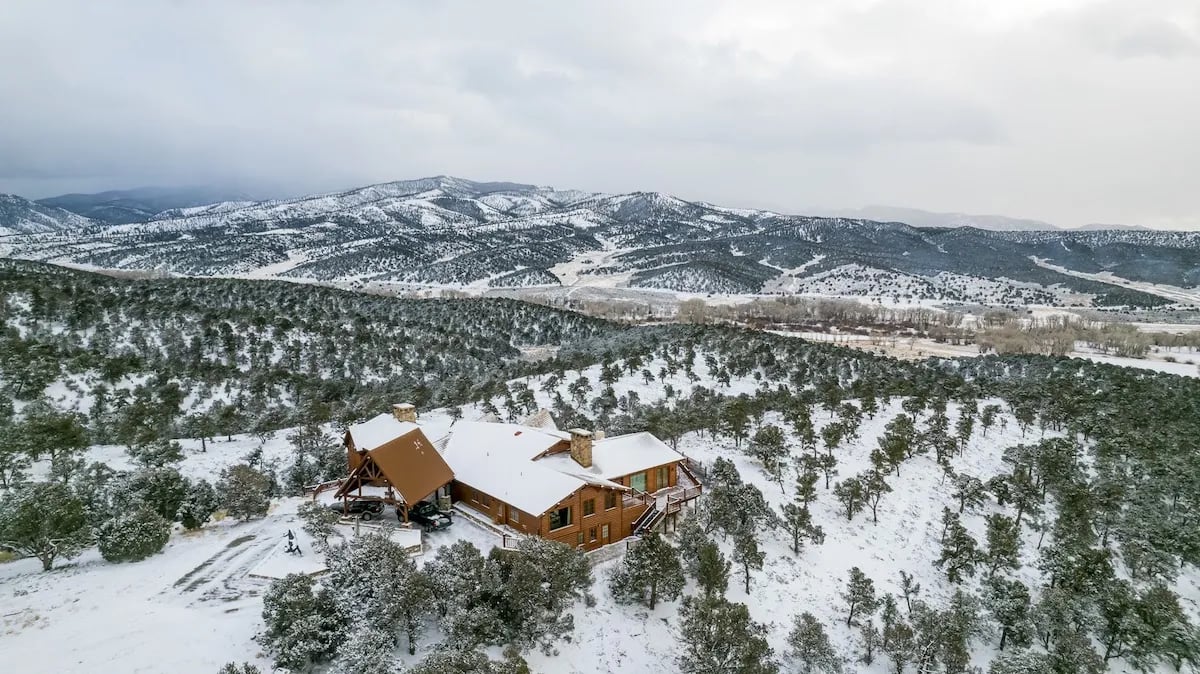 Aerial view of a large lodge complex nestled in a snow-covered forest with mountains
