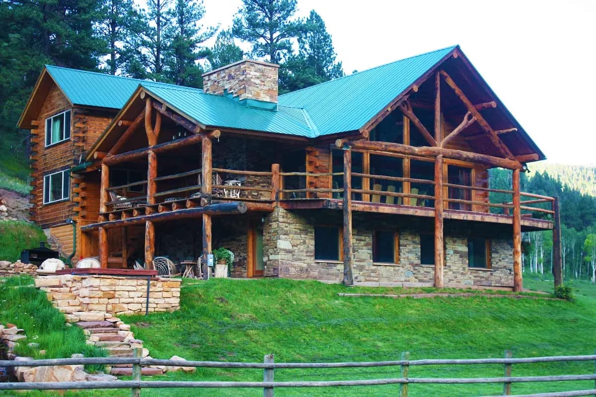 Log cabin lodge with a green roof, stone foundation, and large wrap-around porch