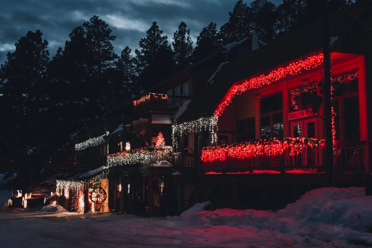 Lodge exterior illuminated with red Christmas lights at night, surrounded by snow-covered trees.