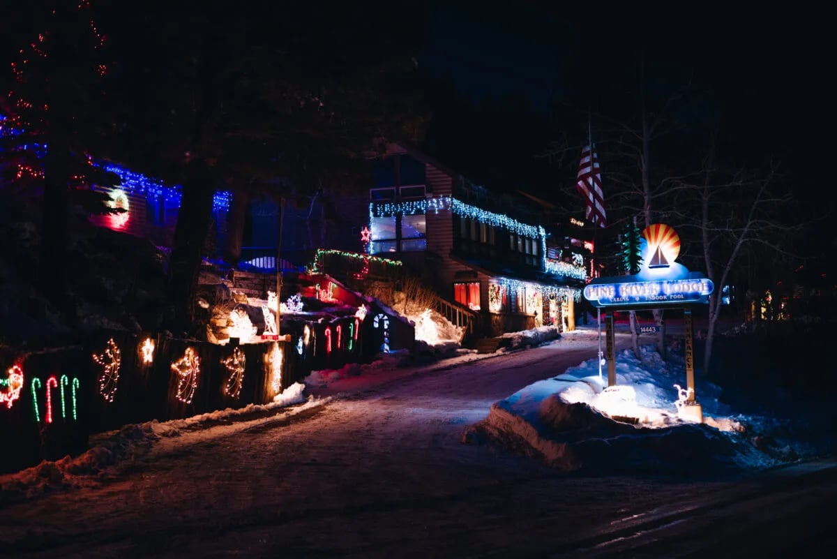 Lodge building entrance decorated with colorful Christmas lights and snow on a winter night.