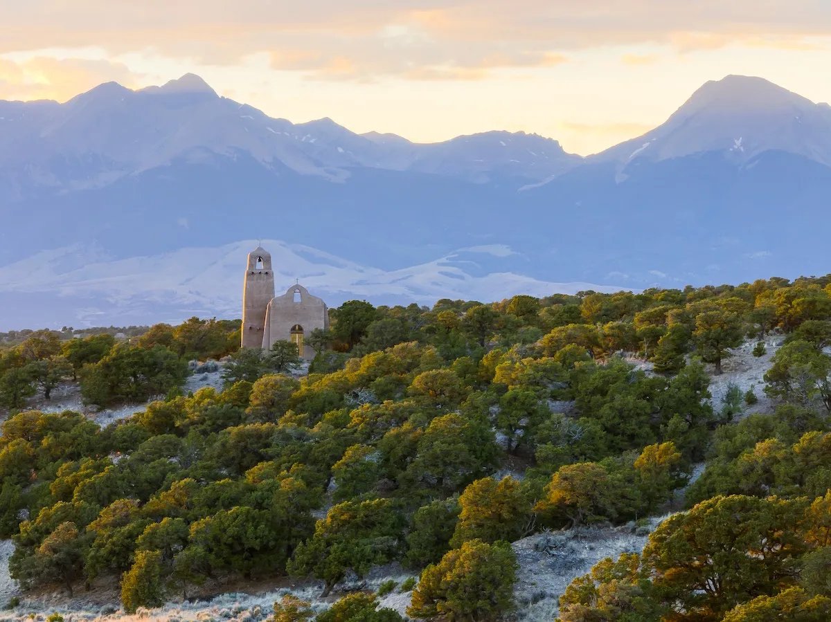Historic stone chapel on a gentle hill with distant snow-capped mountains