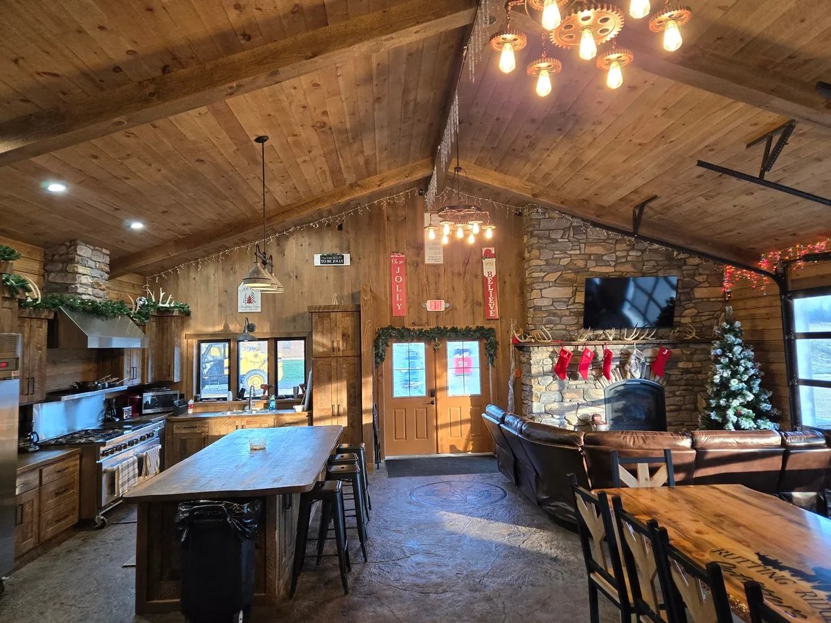 Rustic lodge common area with a kitchen island, dining table, and stone fireplace