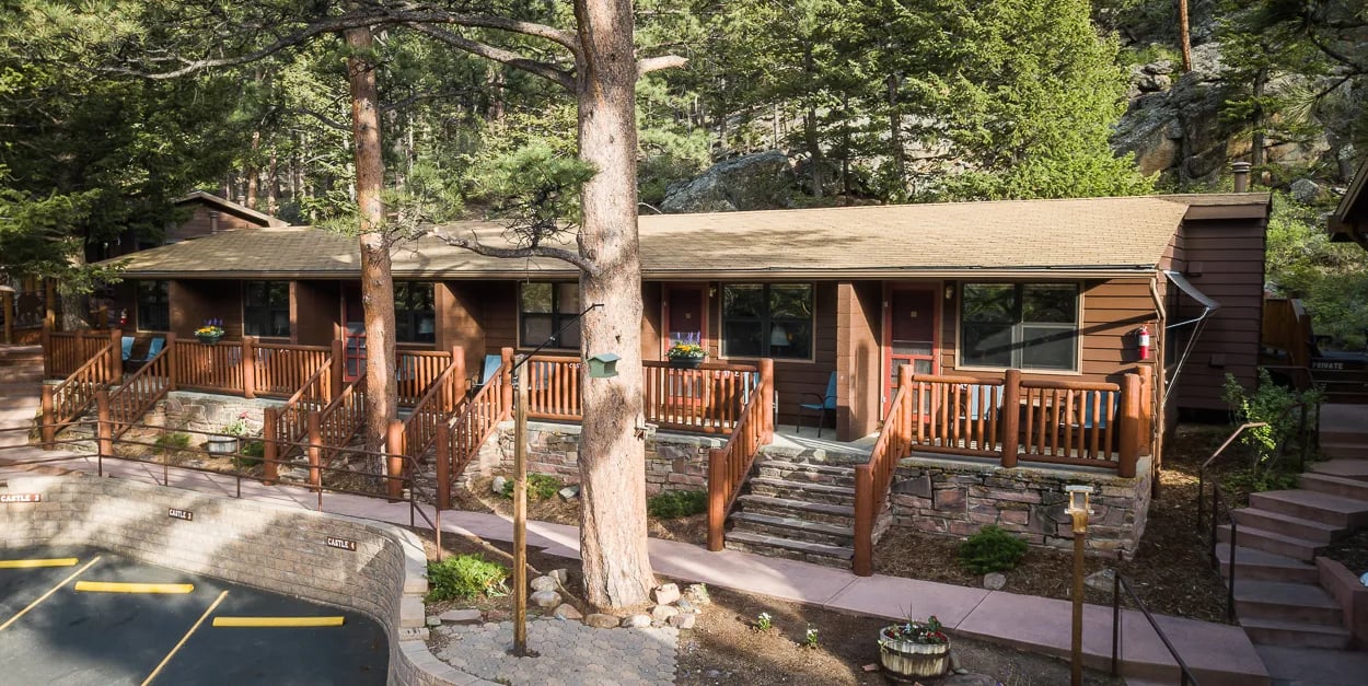 Motel-style lodge building with multiple units and wooden railings surrounded by pine trees