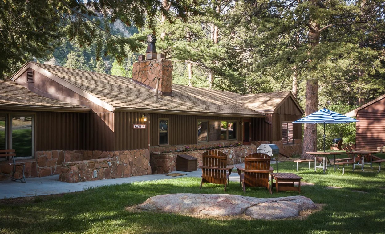 Riverside Cottage exterior with a stone chimney, green lawn, and Adirondack chairs
