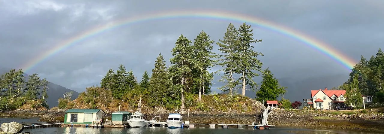 Rainbow arching over the lodge, dock, and forested island on a cloudy day