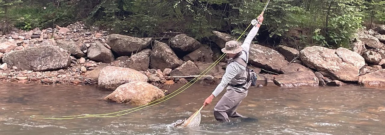 Angler in waders casting a fly rod in a rocky river