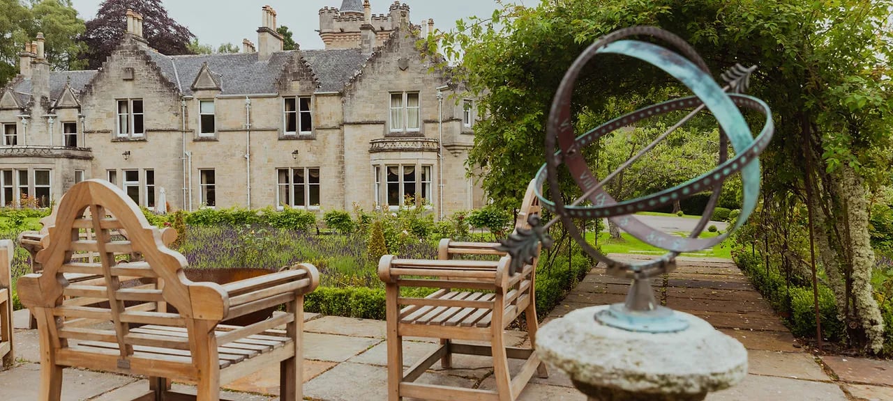 Manicured garden with wooden benches and an armillary sphere, Rothes Glen castle in the background.