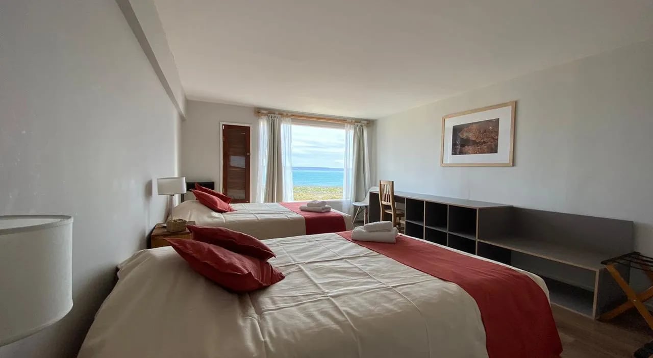 Twin beds in a bright lodge room with a large window overlooking the lake
