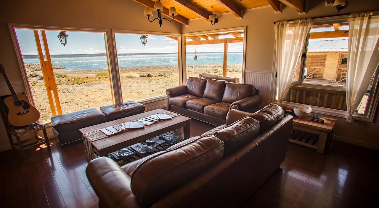 Cozy lodge common area with leather sofas, a coffee table, and large lake-view windows