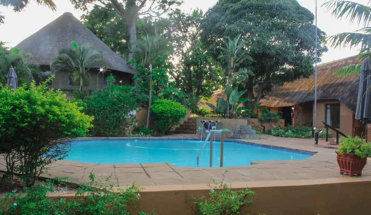Lodge entrance with a thatched roof and manicured bushes, seen from the driveway