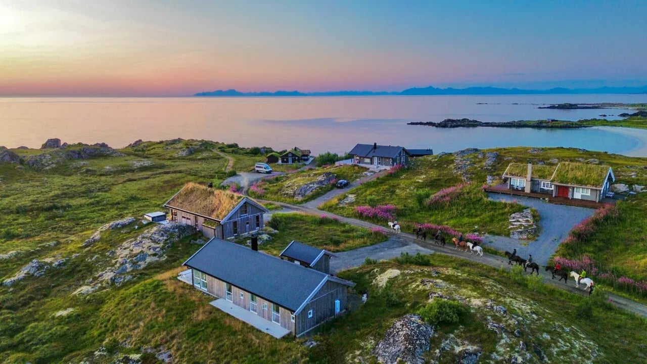 Aerial view of lodges with green roofs nestled in a coastal landscape at sunset