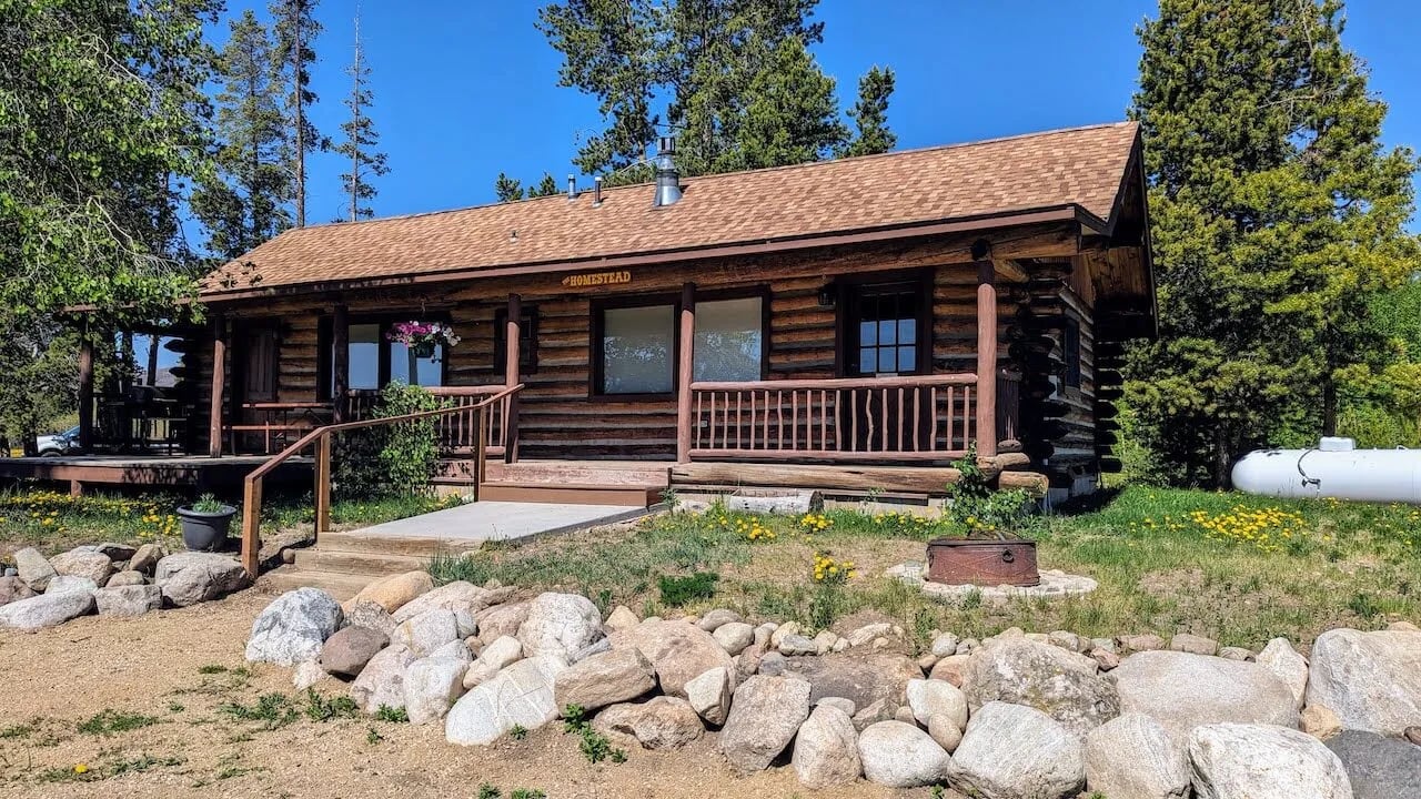 The Homestead log cabin exterior with a covered porch and rock landscaping
